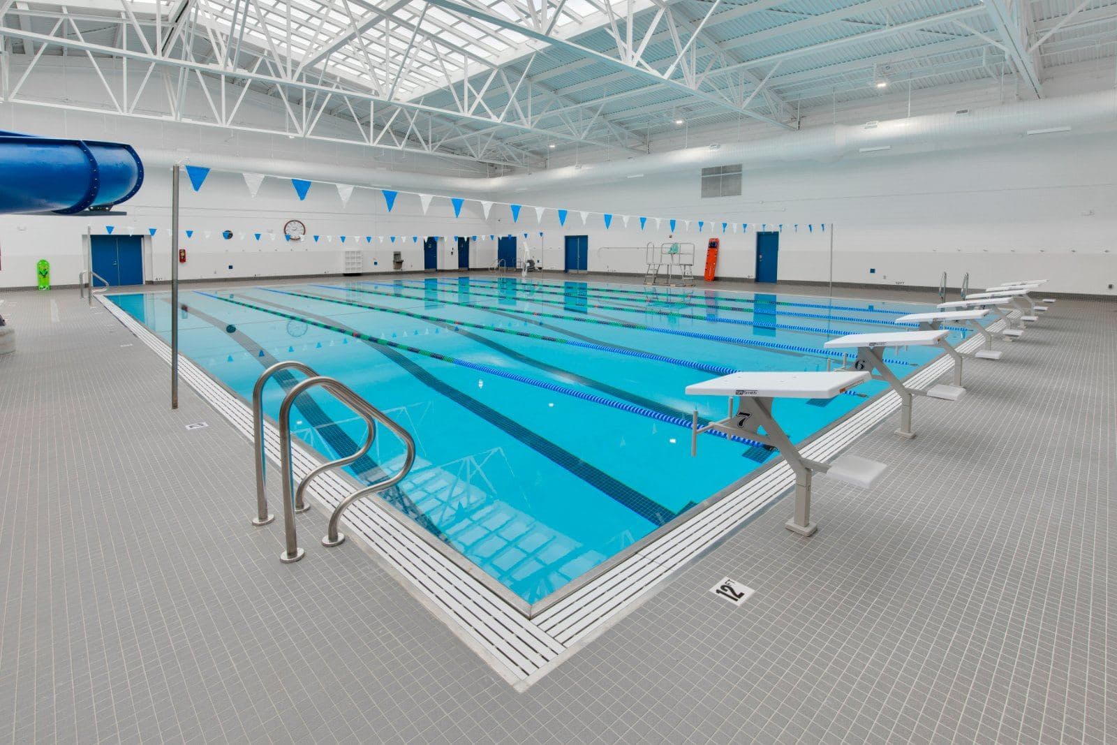 Indoor swimming pool with lap lanes, starting blocks, and an exposed steel roof